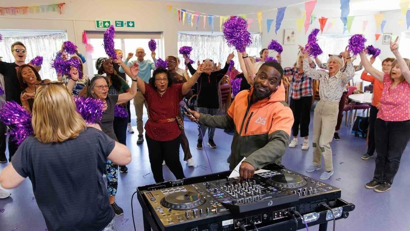 DJ spinning music for a group of seniors dancing with pom-poms at a community event