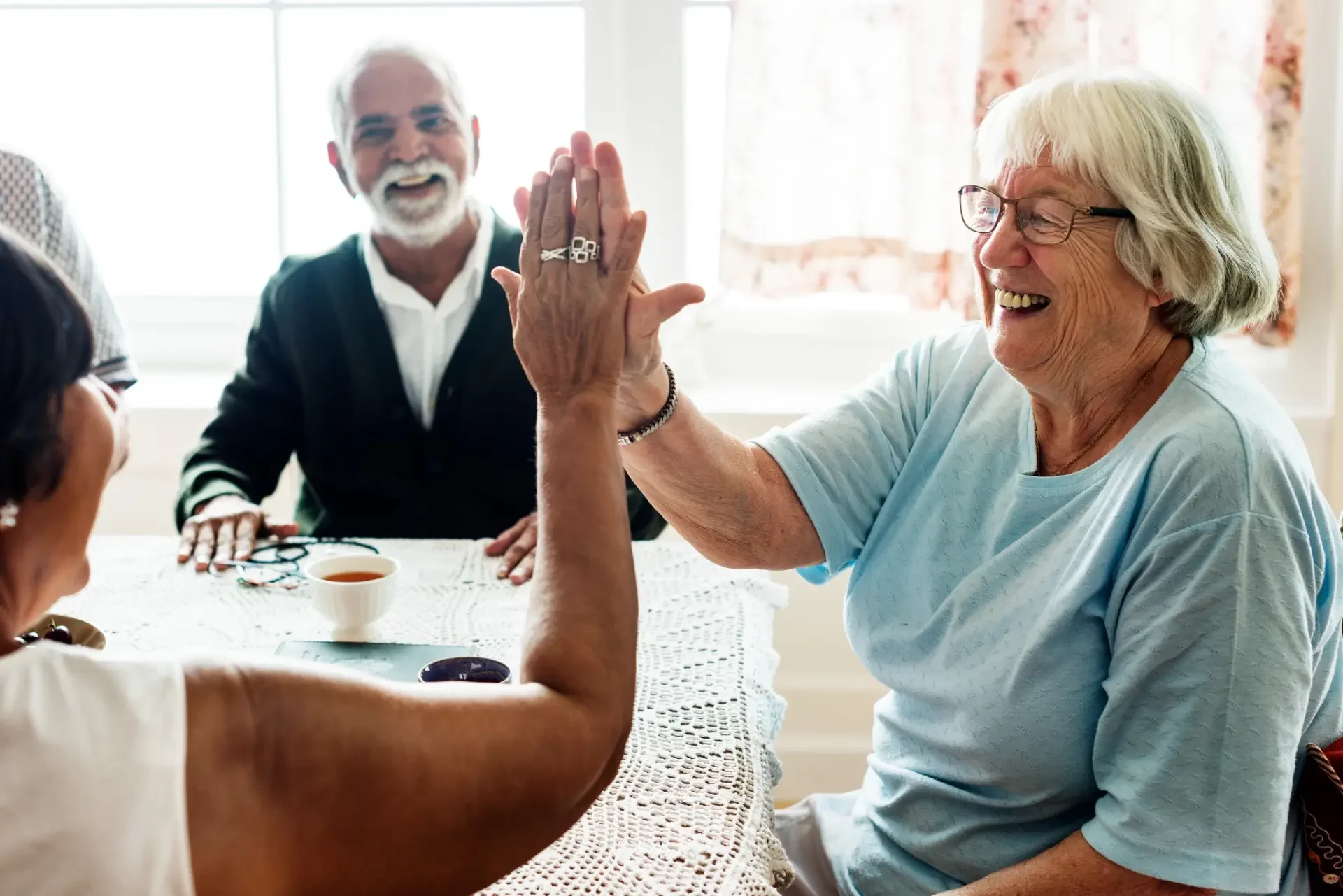 Older adults sharing a joyful high-five around a table.
