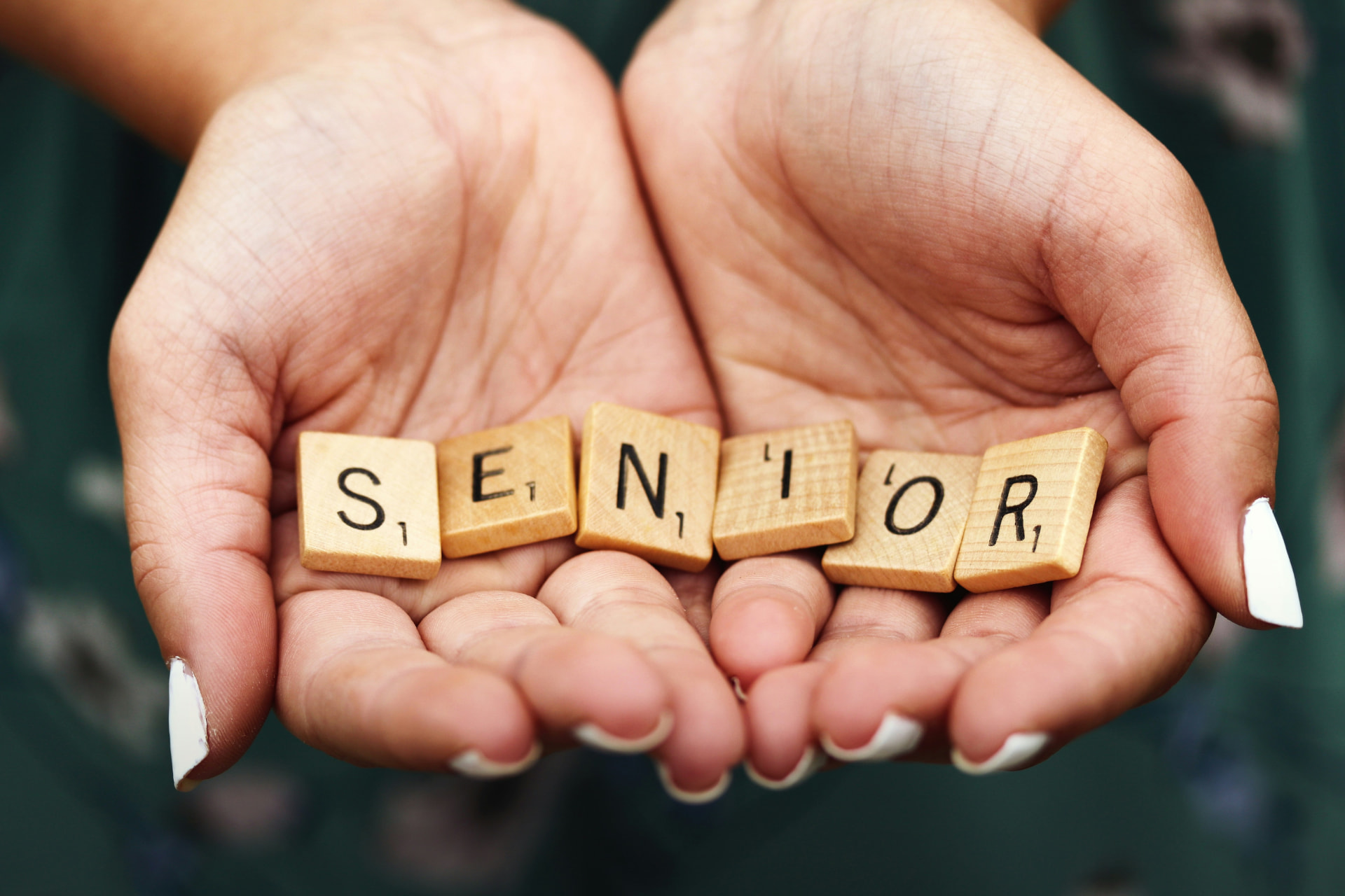 Hands holding wooden letter tiles spelling SENIOR.