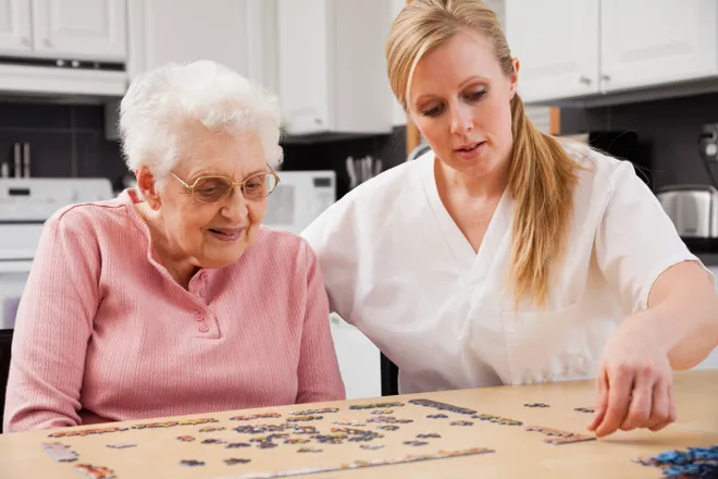 Older adult and caregiver enjoying a jigsaw puzzle together at home.