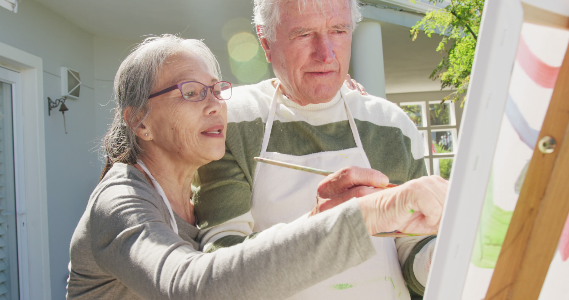 An older couple painting together at an easel at home