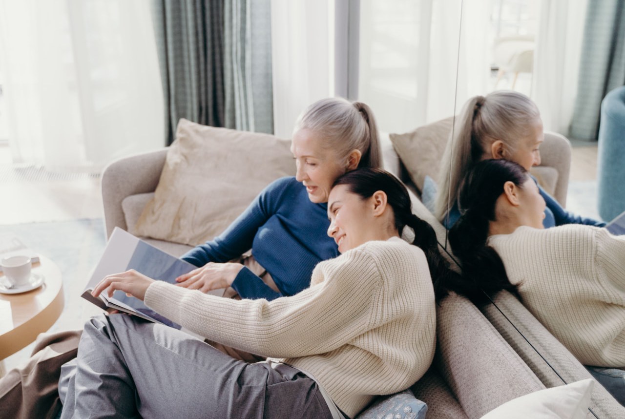 A middle-aged adult daughter and her elderly mother looking at a smartphone together at a kitchen table