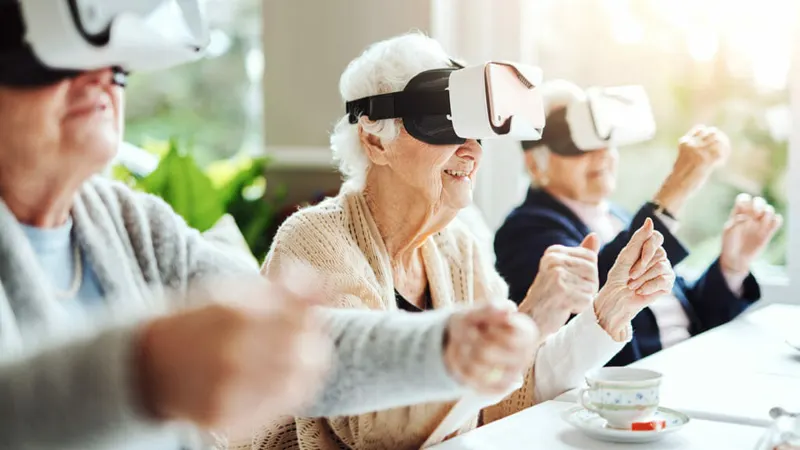 Older women smiling as they explore virtual reality headsets at a table with a teacup